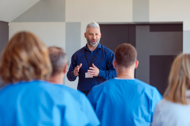 Mature man giving a speech on seminar for medical staff. Group of doctors and nurses sitting in a conference room and listening to male speaker.