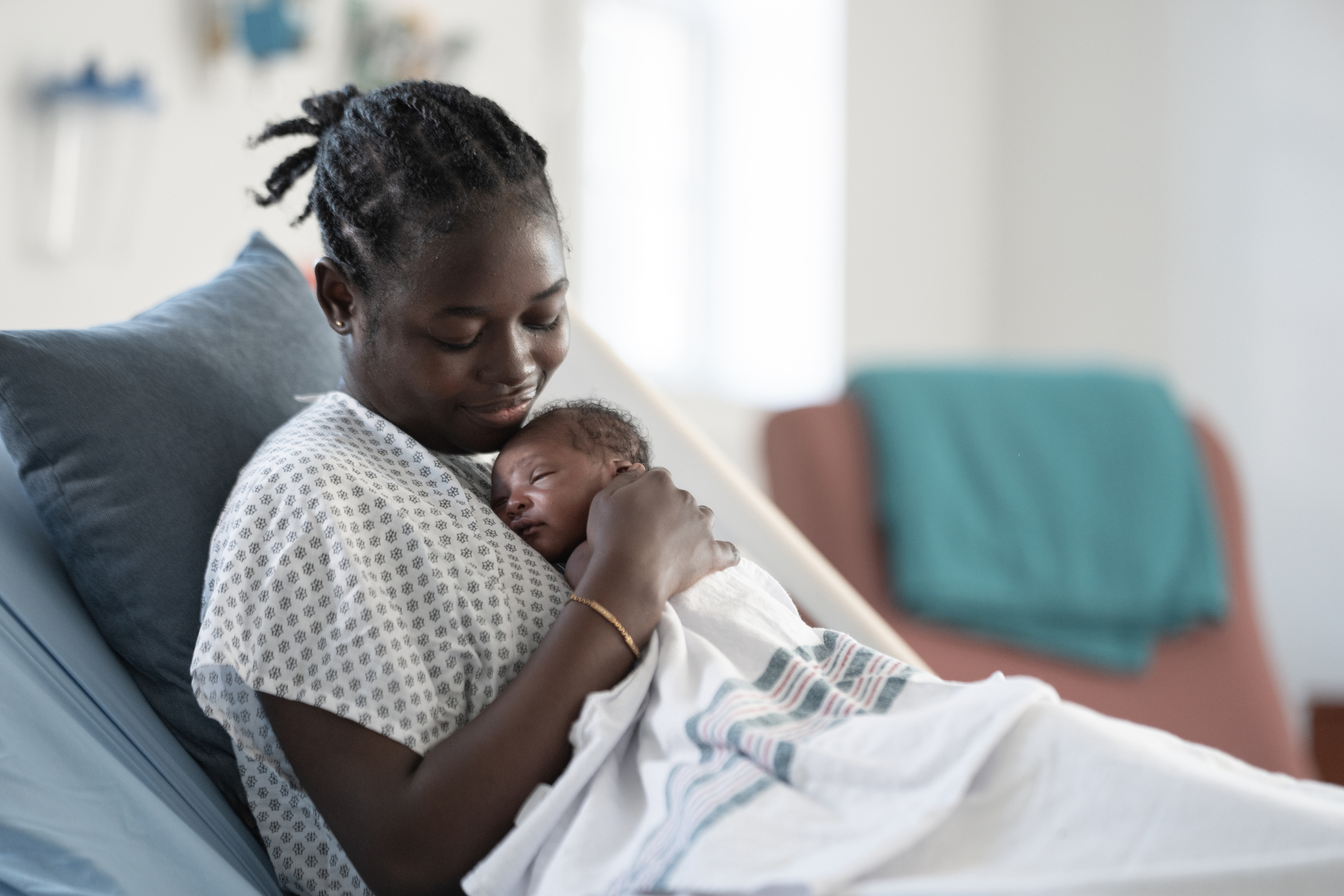 A Black mother gently holds her newborn close in a hospital setting, showcasing tender skin-to-skin bonding and peaceful, intimate family addition during the postpartum moment.